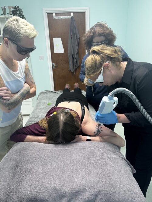 Group of learners in laser safety eyewear observing a practical laser and IPL treatment on a live model