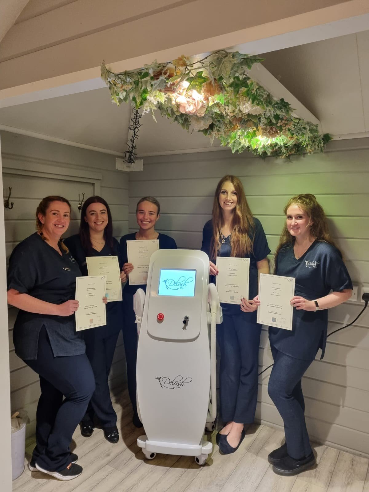 Students holding Focus Awards certificates beside a laser system at Skintastic Aesthetics Training Academy in Southampton